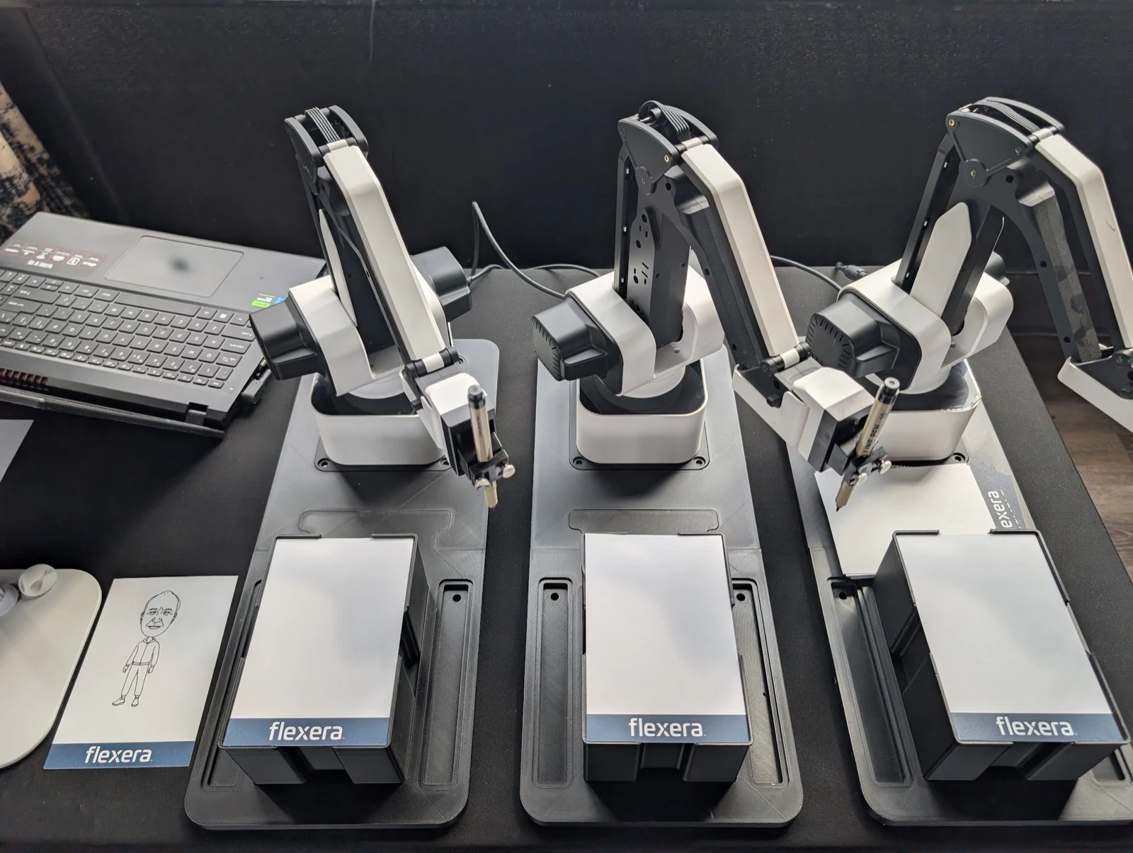 Sketch bot stations with Flexera-branded paper trays drawing caricatures at a corporate event