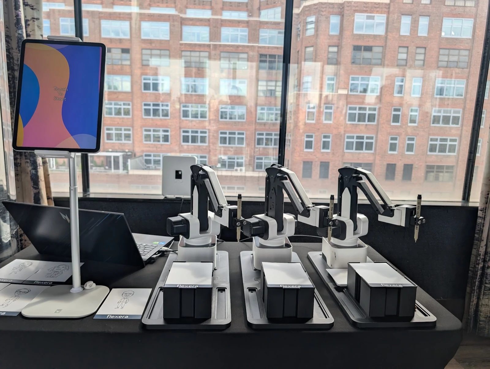 Sketch bot rental NYC — three robot sketch artists with Touch to Start kiosk at a Manhattan corporate event