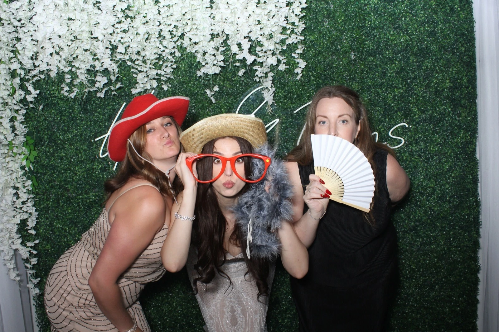 Wedding guests with props at an open air photo booth with greenery backdrop and neon sign