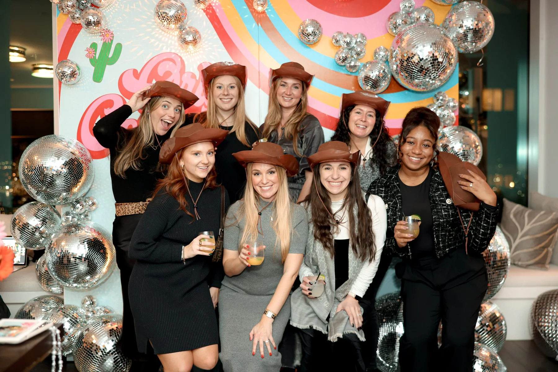 Corporate event photography in NYC: guests posing together in cowboy hats at a Western-themed company holiday party with a disco ball backdrop