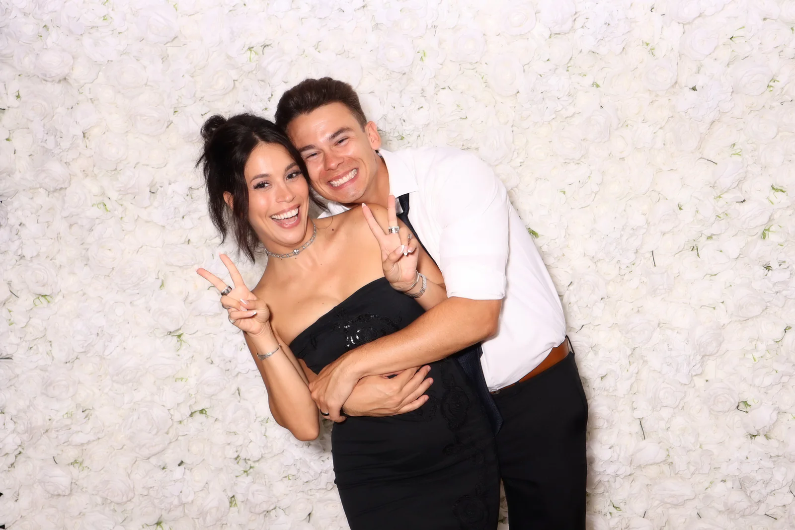 Flower wall photo booth rental NYC — couple posing in front of a white rose flower wall