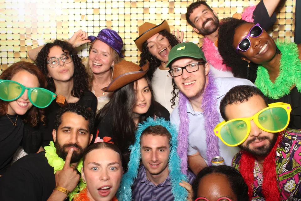 Open air photo booth rental NYC — large group with feather boas at a gold sequin backdrop