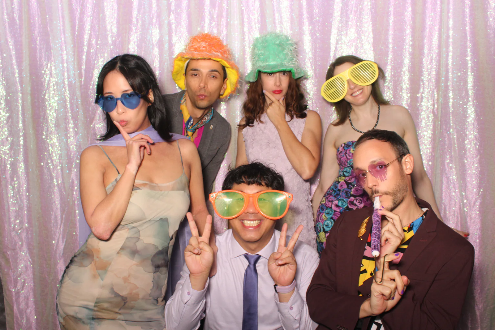 Open air photo booth rental NYC — six guests in fuzzy hats and oversized glasses at an iridescent sequin backdrop