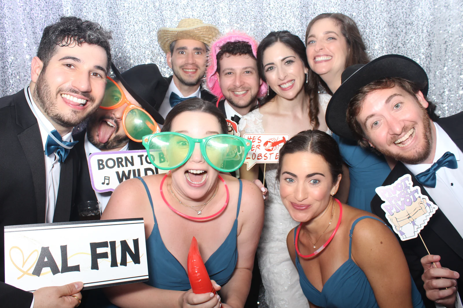 Wedding photo booth rental NYC — bride, groom and bridal party with props at a silver sequin backdrop